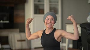 Mujer con cáncer sonriendo y mostrando fuerza con los brazos